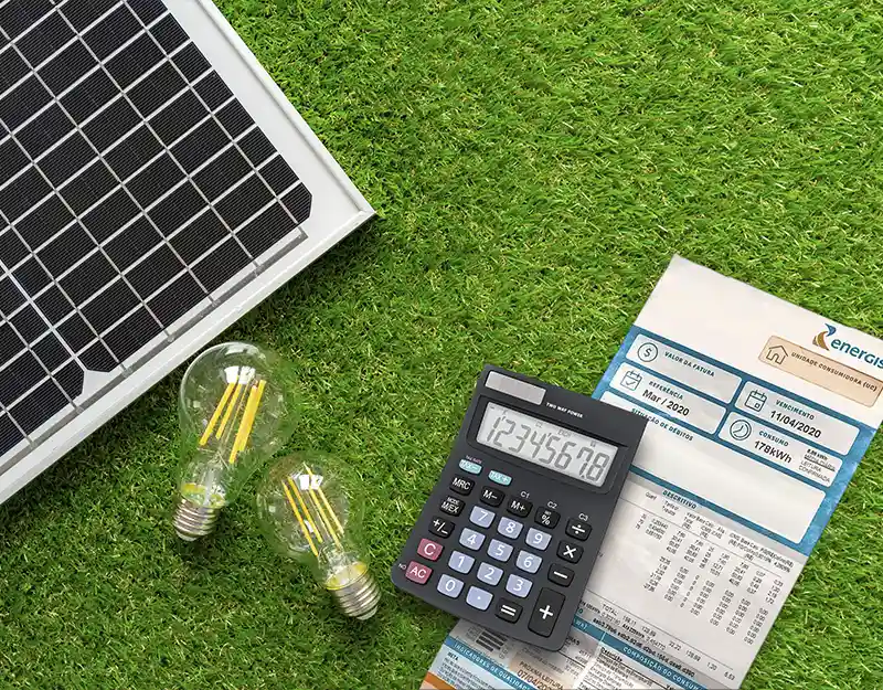 foto de placa solar ao lado de calculadora, lâmpadas amarelas e uma folha de cálculo. Todos os itens sobre uma grama verde